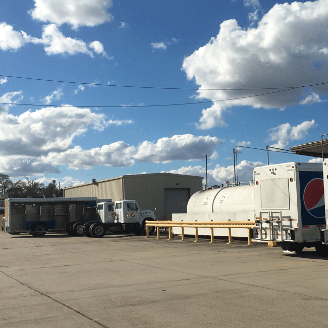 A semi-trailer with a Pepsi logo is parked near an industrial building, where a demolition company offers its remediation services under a partly cloudy sky.