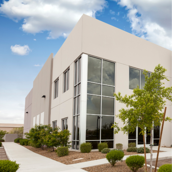 A modern two-story office building with large reflective windows, home to an environmental consulting company, is surrounded by landscaped greenery and a clear blue sky with scattered clouds.