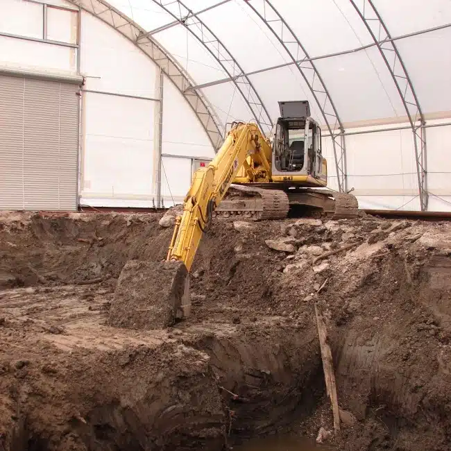 Excavator digging into dirt within a tented structure